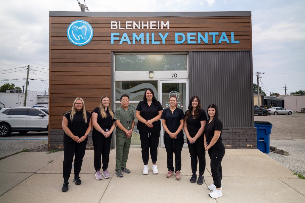 A team of dentists and support staff smiling in front of a dental office outdoors. Contact Us today.